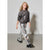 A young girl modeling a two-piece outfit consisting of a dark gray glittery sweatshirt and shiny metallic silver pants, paired with black boots, against a plain light gray studio background.
