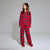 A young girl wearing a red and black plaid pajama set with matching red slipper socks, standing against a light gray studio background.