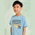 A young boy smiling and wearing a light blue t-shirt with 'MISSISSIPPI Jackson EST. 78' printed on the front, set against a soft, pale green background.