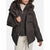 A woman wearing a dark brown puffer jacket with a plush brown faux-fur lined hood and cuffs, paired with a cream ribbed turtleneck and cream pants, shown against a plain white background.