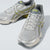 A pair of ASICS athletic sneakers in metallic silver with yellow-green stripe accents and a gray collar, shown on a light gray studio background.