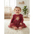 A baby girl sitting on a cream rug in a bright nursery, wearing a burgundy long-sleeve dress with a tulle skirt and a 'Haul of Joy' lion graphic on the front.