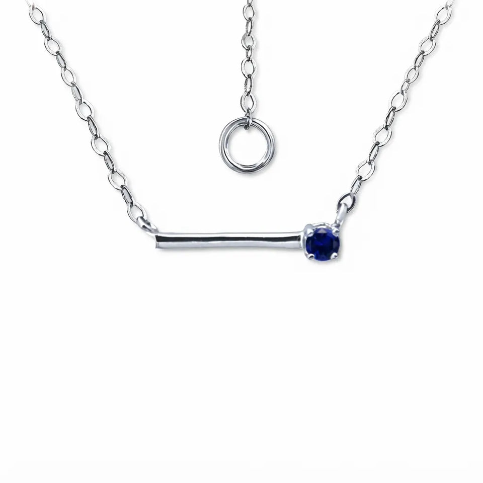 A silver bar necklace with a single deep blue gemstone pendant, displayed on a clean white background with an inset showing the adjustable ring clasp.