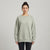 A woman modeling a sage green crewneck sweatshirt with textured lace-knit sleeves, paired with black leggings, against a light gray studio background.