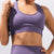 A close-up of a model wearing a textured, ribbed purple sports bra and matching high-waisted leggings against a light gray studio background.