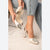 A person wearing off-white pointed-toe slingback high heels with crystal embellishments on the toes, with one shoe being removed and held. The person is wearing light-wash blue jeans.