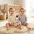 Two toddlers sitting on a fluffy cream rug in a bright nursery, wearing matching long-sleeve pajamas. The child on the left wears a cream and beige striped top with a small white heart graphic, and the child on the right wears a light lavender-gray top with white cloud prints.