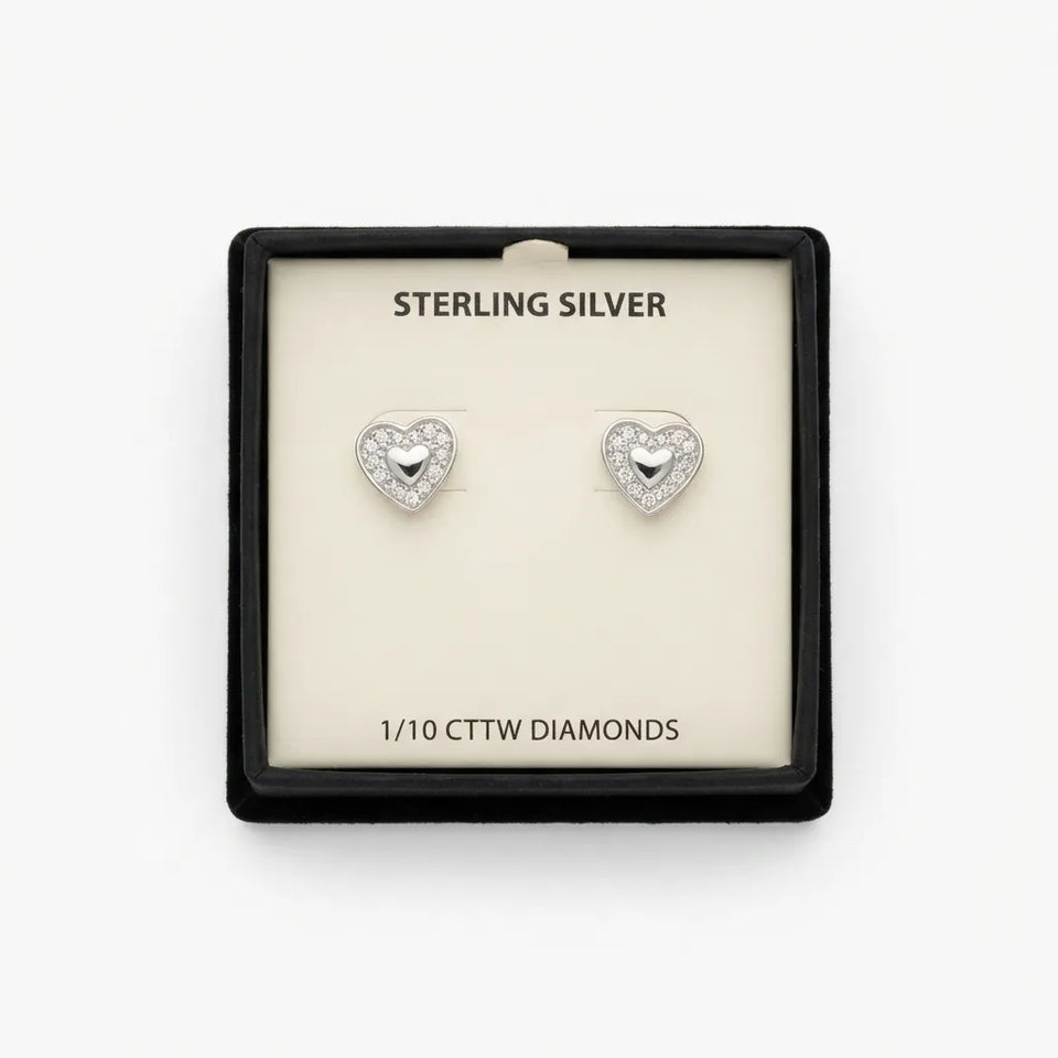 A pair of sterling silver heart stud earrings with inlaid clear stones, presented in a black square jewelry box with a cream insert. The insert reads 'STERLING SILVER' and '1/10 CTTW DIAMONDS'.