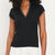 A woman wearing a black short-sleeve V-neck knit top with thin white piping trim along the neckline and sleeve cuffs, paired with white bottoms, against a plain light background.