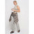 A woman models a sleeveless black and white striped top with a patterned neck scarf, light gray wide-leg jeans, and a beige plaid shirt tied around her waist, holding a white coffee cup against a light gray studio background.