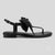 A black flat thong sandal with a wide strap, a matching ankle strap, and a large decorative bow embellished with silver studs on the toe post, shown against a light gray background.