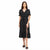 A woman modeling a black midi wrap dress with white polka dots, short puff sleeves, and a front slit, paired with black slide sandals against a plain white background.