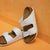 A pair of white double-strap slide sandals with cork-look midsoles, photographed against a warm orange textured wall and floor.