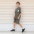 A child model wearing a matching gray short-sleeve t-shirt and shorts set with a retro handheld game console graphic on the chest, standing against a beige horizontal-slat wall.