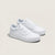 A pair of classic low-top platform sneakers in all white, featuring a thick white rubber sole, white laces, and the signature side stripe, set against a solid light beige background.