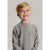 A young boy with blonde hair smiling, wearing a heather gray long-sleeve crewneck sweatshirt with a small horizontal logo on the left chest, set against a plain light gray background.