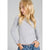 A young blonde girl wearing a light gray ribbed long-sleeve top with a raw, frayed hem and cuffs, paired with blue jeans, shown against a plain gray background.