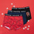 Three pairs of Rosemary Christmas-themed boxer briefs arranged in an overlapping fan on a bright red background with white snowflake decorations. The red pair features a Christmas light pattern, the navy pair is solid navy, and the black pair has a 'Ho Ho Ho' graphic.