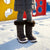 A child standing in snow wearing dark gray quilted winter boots with brown faux-fur trim and gray leggings, with a playground in the background.