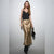 A woman modeling a black camisole top and a shiny metallic gold satin midi skirt, holding a small black handbag against a plain light gray studio background.