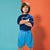 A young boy modeling a blue athletic t-shirt and matching light blue shorts, standing against a split teal and orange studio background.