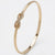 A polished gold bangle bracelet featuring a central infinity symbol paved with small clear stones, set against a clean white background.