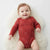 A baby lying on a white faux fur rug, wearing a rust red long-sleeve bodysuit with a small white floral pattern.