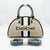 A beige dome-shaped handbag with black trim, two vertical white stripes, and the word 'bebe' printed in black across the front. The handles are wrapped in protective plastic, and a matching wrapped shoulder strap is placed in front on a light gray background.
