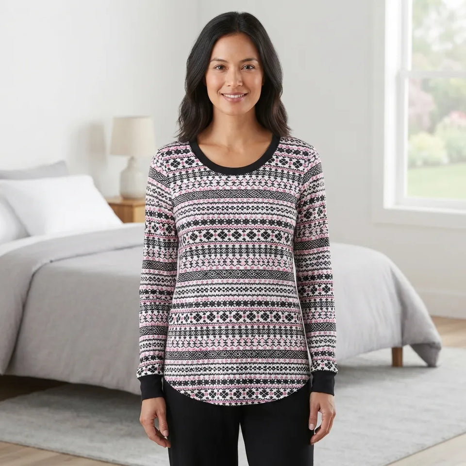 A woman wearing a long-sleeve crewneck top with a black, white, and pink Fair Isle pattern, standing in a brightly lit bedroom.