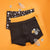 Three pairs of boy's boxer briefs laid flat on an orange background. The front pair is black with a skeleton-and-pumpkin graphic on the right leg.