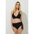 A blonde model wearing a black two-piece bikini with a wrap-front top and side-tie bottoms, standing against a light gray studio background.