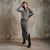 A woman models a gray knit two-piece set consisting of a long-sleeve cropped top and a matching high-slit midi skirt, paired with black knee-high boots, set against a textured concrete wall.
