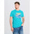 A man wearing a bright turquoise graphic t-shirt with a 'West Coast' car design and blue jeans, standing against a light gray studio background.