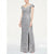 A woman modeling a floor-length silver sequined gown with an off-the-shoulder neckline, fitted silhouette, and front slit, photographed against a plain light gray studio background.