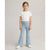 A young girl stands against a light gray studio background wearing a white short-sleeve t-shirt, light blue flared jeans with heart-shaped knee patches, and white sneakers.