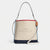 A Coach New York canvas bucket bag in beige, navy, and light blue with a red top trim, featuring a silver-tone horse bit logo and a brown leather hangtag, shown on a light gray background.