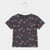 A kids' short-sleeve t-shirt in dark gray, featuring an all-over print of cartoon monsters with pink bows, black eyes, and white fangs, hanging on a white plastic hanger against a light gray background.