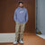 A man wearing a heathered periwinkle blue hoodie with a white chain logo on the chest, paired with beige cargo pants and white sneakers, standing in a studio setting with a brown backdrop.