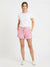 A woman modeling pink and white patterned shorts with a white t-shirt and white sneakers, standing against a plain white studio background.