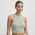 A woman modeling a light sage green ribbed crop top against a plain light gray studio background.