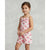 A young girl modeling a light pink sleeveless romper with a watermelon print, set against a neutral gray studio background.