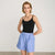 A model wearing a black tank top and blue and white striped shorts, standing against a light gray studio background.