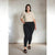 A woman modeling a beige short-sleeve V-neck top and black skinny jeans against a textured concrete wall.