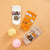 Three pairs of ankle socks with cute cartoon mouse Halloween designs, displayed on a warm peach background alongside two small decorative bath bombs.
