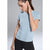 A woman wearing a light blue short-sleeve crewneck athletic top and black leggings, posing against a neutral gray studio background.