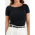 A woman wearing a black short-sleeve top with a gold chain detail along the boat neckline, paired with white pants and a black belt.