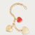 A gold-tone heart charm bracelet featuring three heart charms: two polished gold heart pendants and one smaller red heart charm, displayed on a light gray background.