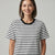 A woman wearing a black and white horizontally striped short-sleeve t-shirt with a solid black crew neck, photographed against a neutral light gray background.