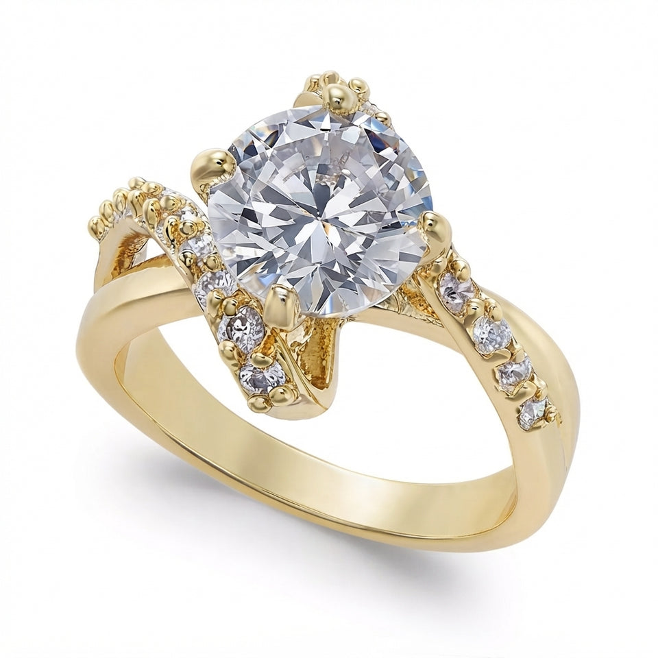 A yellow gold engagement ring featuring a large round brilliant-cut clear center stone, accented by small pavรฉ-set clear stones along the curved shoulders and a split shank, shown on a white background.