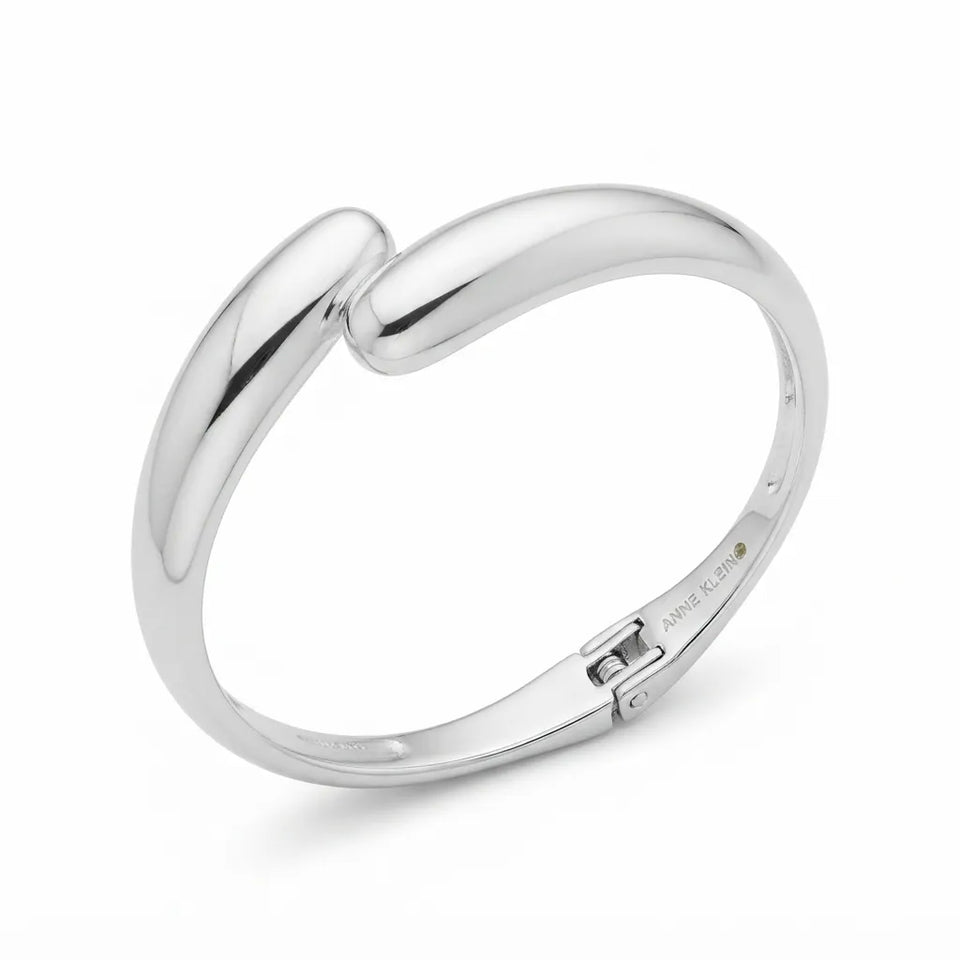 A polished silver-toned metal bangle bracelet with a unique curved, interlocking design and a sliding clasp, shown on a clean white background.